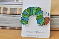 Glitter caterpillar brooch on backing card against timber and book background
