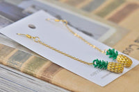 Pineapple dangle earrings laid diagonally across display card and books