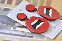 Close-up of red lips earrings showing glossy perspex finish and black outline detail