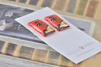 Close-up angled view of two glossy resin ramen packet stud earrings on backing card