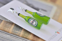 Close-up angled view of two beer bottle earrings showing label and glossy resin finish