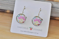 Round silver-toned dangle earrings with pink and gold flower design on Kaboodle Designs card