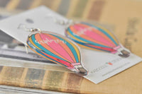 Hot air balloon drop earrings lying on Kaboodle Designs card, angled view showing glossy acrylic finish