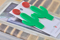 Angled view of two green cactus earrings showing laser-cut arm detail and silver jump rings
