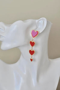 Red heart drop earring worn on ear, showing graduated heart sizes and gold-tone edging