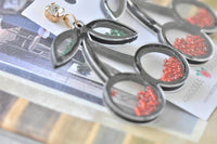 Close-up of cherry earring showing loose beads inside acrylic outline and gold hook detail