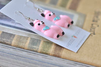 Pair of pink llama earrings lying flat showing glossy resin finish and black hooves
