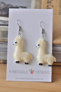 Pair of beige resin llama drop earrings on a Kaboodle Designs card, front view