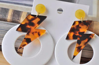 Pair of leopard-toned lightning bolt earrings with white hoops laid flat on backing card