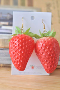Pair of large 3D red strawberry drop earrings on white card with green leaf detail