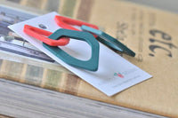 Pair of linked geometric resin earrings laid on card against book stack
