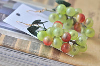 Close-up angled view of grape earrings with leaf detail resting on a wooden surface