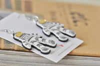 Close-up of layered acrylic astronaut earrings showing line-drawn suit detail and gold visor