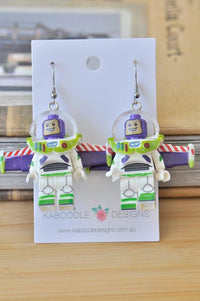 Pair of space ranger figure drop earrings on Kaboodle Designs card, front view showing helmet and wings