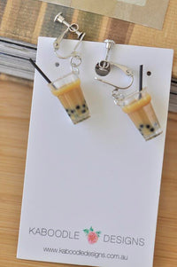 Bubble tea clip-on earrings on card against wooden background, front view