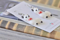 Close-up of white resin alpaca earrings lying flat showing glossy finish and black hoof detail