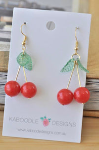 Pair of red cherry drop earrings with green leaves on a Kaboodle Designs card
