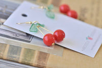 Close-up of glossy red cherry beads and leaf detail resting on earring card