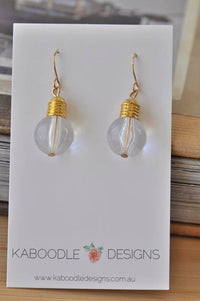 Clear resin lightbulb earrings with gold-tone cap and filament detail on jewellery card