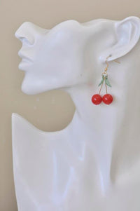 Cherry earring worn on ear, close-up side view showing gold stem detail