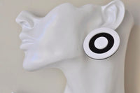 Black and white circle target earring worn on ear, close-up side view on model