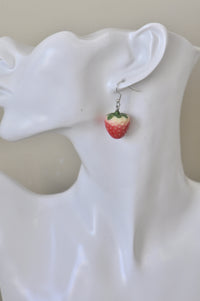 Close-up of single strawberry earring worn on ear showing glossy red and cream detail