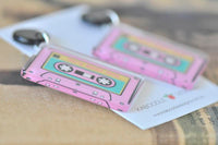 Close-up of two pink cassette tape earrings showing printed detail and clear acrylic edges