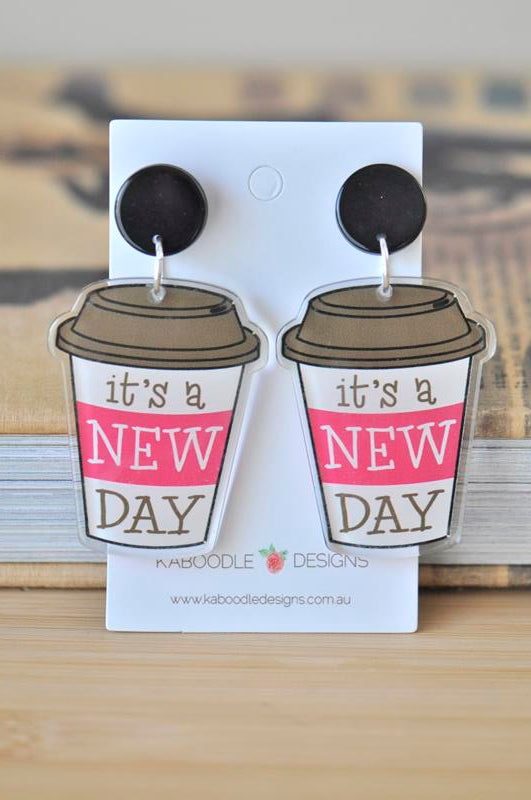 Pair of coffee cup dangle earrings printed with 'it's a NEW DAY' on a display card