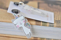 Close-up of rainbow cat unicorn earring resting on stacked books beside packaging