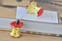 Close-up of two apple core earrings resting on a book, showing seed and stalk detail
