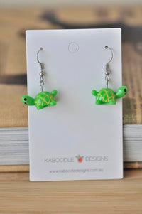 Green resin turtle drop earrings with gold shell detail on white display card
