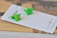 Close-up of two green resin turtle earrings resting on Kaboodle Designs card