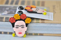 Single Frida Kahlo earring with red and yellow roses and yellow bead, propped on books