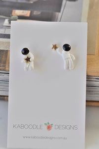 White enamel astronaut stud earrings on card, one holding a gold star, one reaching for it