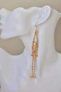 Gold skeleton earring worn on ear, showing full length and skull detail