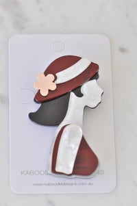 Acrylic brooch of a retro lady in profile wearing a red hat with white trim and pink flower, on backing card