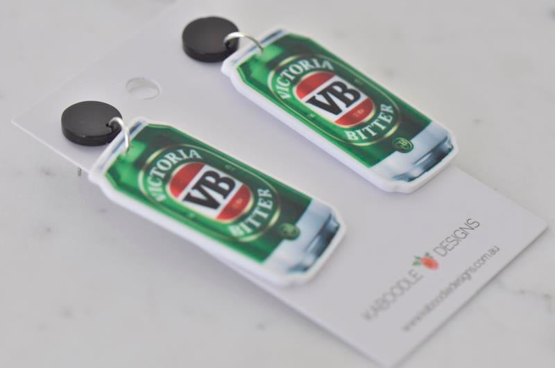 Close-up angled view of two green and red VB beer can shaped earrings with black studs