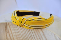 Mustard yellow striped chiffon headband with centre knot, angled view on wood surface