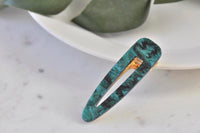 Emerald green marbled acrylic barrette clip with gold fastening, angled view on marble surface