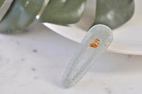 Silver glitter acrylic barrette clip standing upright against a leafy background