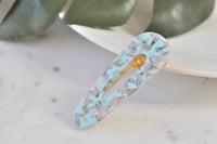 Teal and pink swirl acrylic barrette hair clip, angled view on marble surface