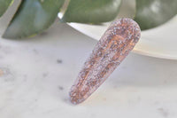 Purple glitter acrylic barrette clip standing upright against a leafy background