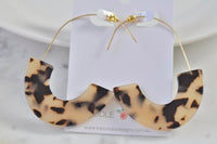 Pair of curved acrylic hoop earrings on card, showing full leopard pattern and gold wire hooks