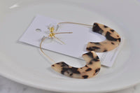 Overhead view of leopard print hoop earrings laid flat on card beside a white plate