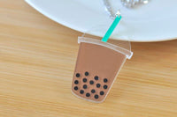 Side angle of boba cup pendant necklace resting on wooden surface with plate in background