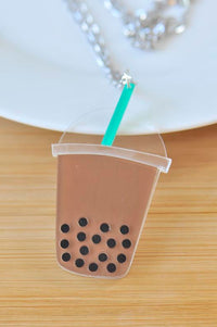 Acrylic boba milk tea cup pendant with green straw and black tapioca pearls, close-up on wooden surface
