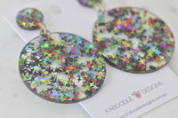 Angled close-up of two glitter star resin circle earrings showing star detail