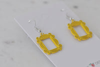 Angled view of two yellow frame drop earrings with silver hooks on card