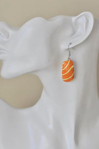 Orange striped salmon sashimi ceramic earring worn on ear, close-up side view