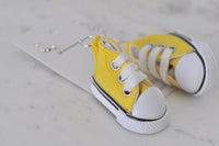 Close-up of yellow sneaker earring showing white laces, toe cap and black stripe trim
